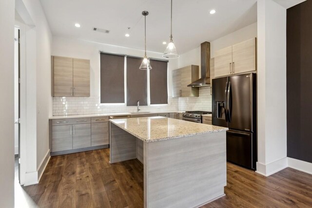 kitchen with a center island, stainless steel appliances, wall chimney range hood, light stone counters, and dark hardwood / wood-style flooring