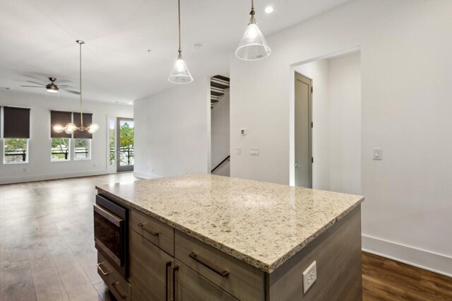 kitchen with dark hardwood / wood-style flooring, light stone counters, stainless steel microwave, and a center island