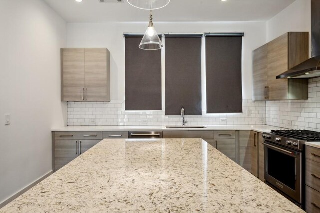 kitchen with wall chimney range hood, sink, high end stainless steel range, light stone countertops, and decorative light fixtures