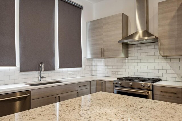 kitchen featuring light stone countertops, appliances with stainless steel finishes, tasteful backsplash, wall chimney exhaust hood, and sink