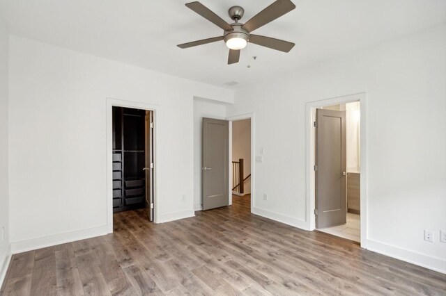 unfurnished bedroom featuring ensuite bath, a spacious closet, light hardwood / wood-style flooring, and ceiling fan