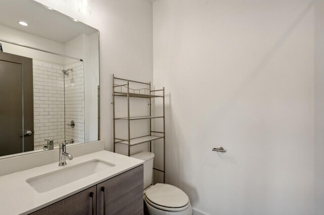 bathroom featuring a tile shower, vanity, and toilet