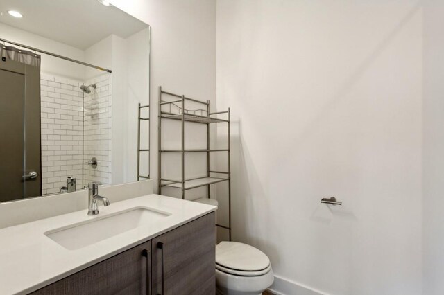 bathroom with a tile shower, vanity, and toilet