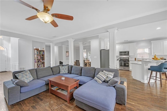 living room featuring dark wood-type flooring, ceiling fan, sink, and ornate columns