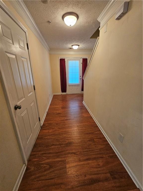 corridor with a textured ceiling, crown molding, and dark wood-type flooring