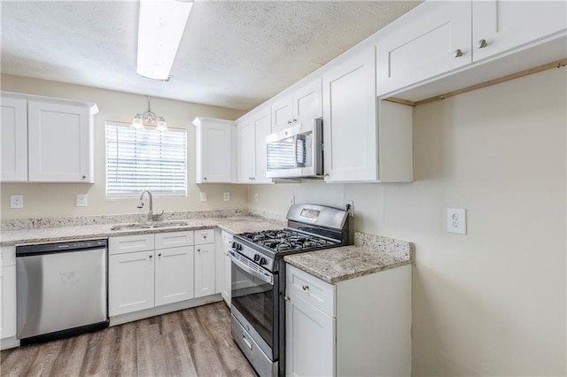 kitchen with light wood-type flooring, a sink, a textured ceiling, stainless steel appliances, and white cabinets