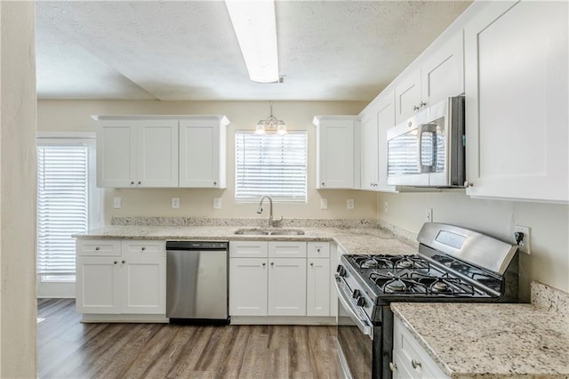 kitchen featuring light wood-type flooring, appliances with stainless steel finishes, a textured ceiling, white cabinetry, and a sink