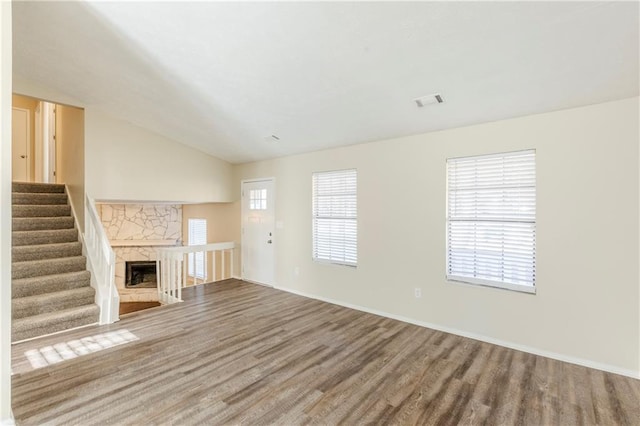 unfurnished living room with wood finished floors, visible vents, lofted ceiling, a fireplace, and stairs