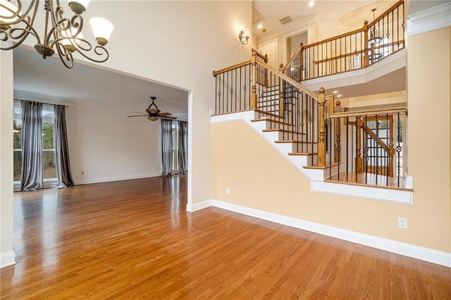 staircase featuring hardwood / wood-style floors, ceiling fan with notable chandelier, and a high ceiling