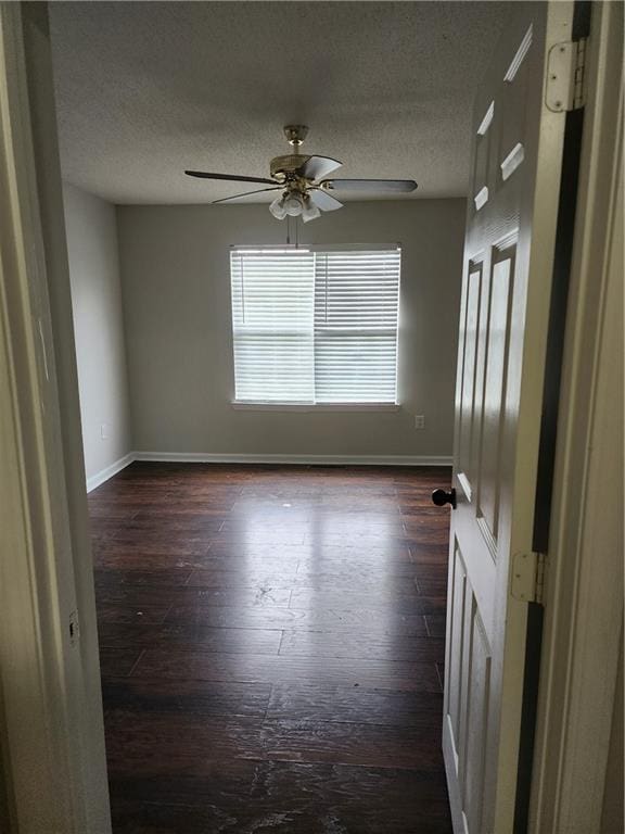 empty room with a textured ceiling, dark wood finished floors, baseboards, and a ceiling fan