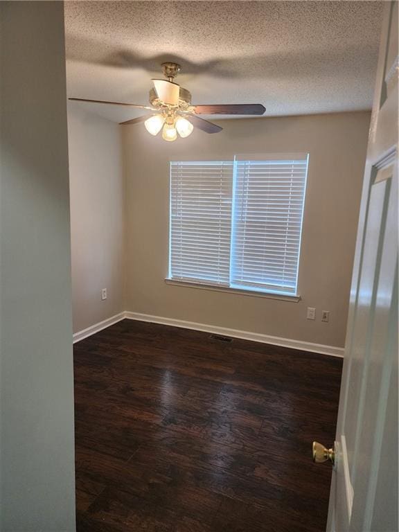 empty room with a textured ceiling, dark wood-style flooring, ceiling fan, and baseboards