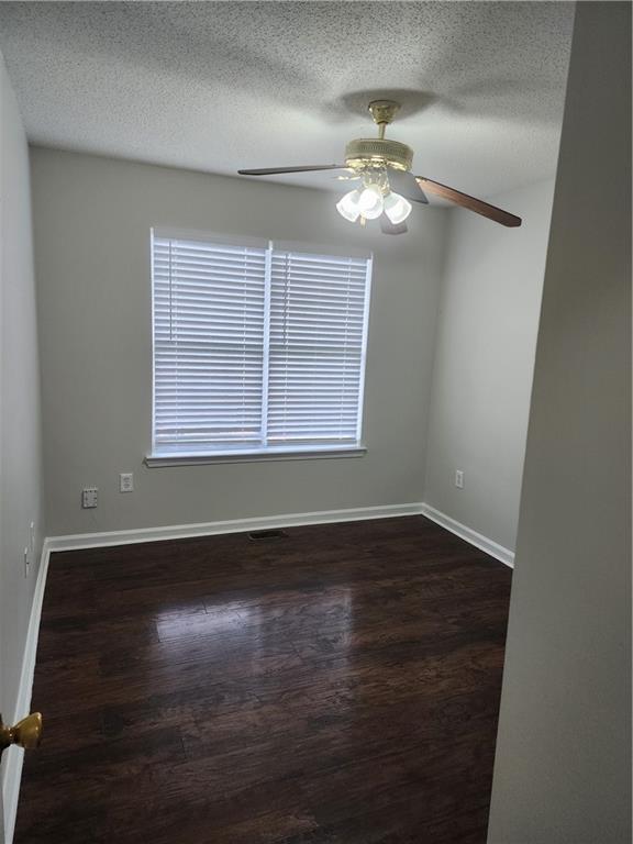 unfurnished room with a textured ceiling, baseboards, a ceiling fan, and dark wood finished floors
