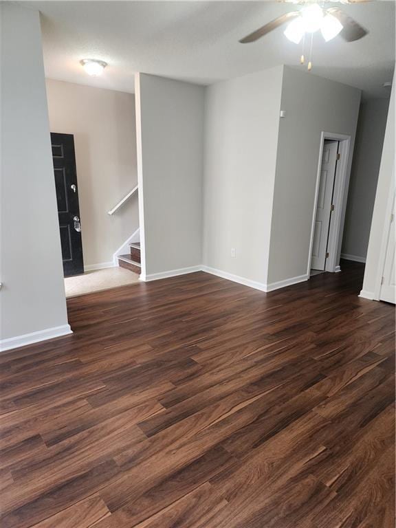 empty room featuring stairs, baseboards, a ceiling fan, and dark wood finished floors