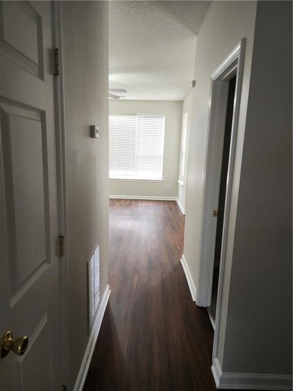 hall with visible vents, a textured ceiling, baseboards, and dark wood-style floors