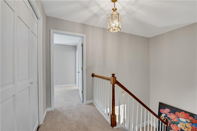 corridor with a chandelier, baseboards, light carpet, and an upstairs landing