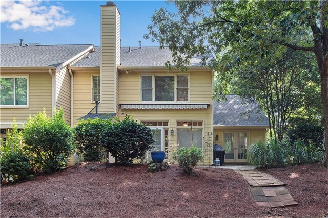 rear view of property with a shingled roof, a chimney, and french doors