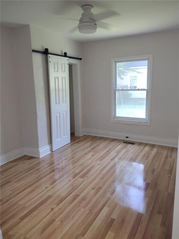 747 Bowman St, Macon, GA 31217 - unfurnished bedroom with a barn door, light wood-type flooring, and ceiling fan