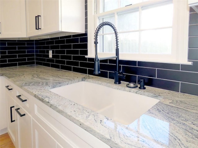 details with backsplash, white cabinetry, light stone countertops, and sink