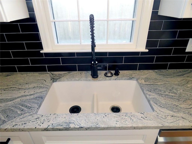 details with white cabinets, light stone counters, and sink