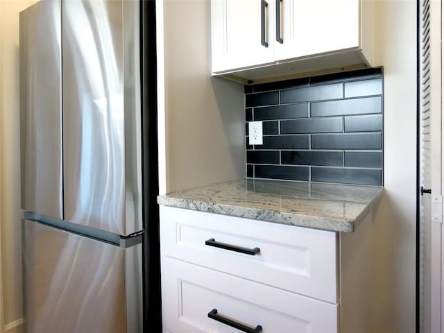 kitchen with backsplash, stainless steel refrigerator, light stone countertops, and white cabinets