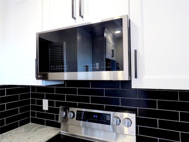 room details with light stone countertops, range, tasteful backsplash, and white cabinetry