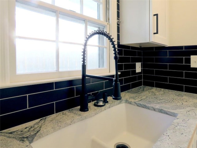 room details with decorative backsplash, light stone counters, sink, and white cabinets