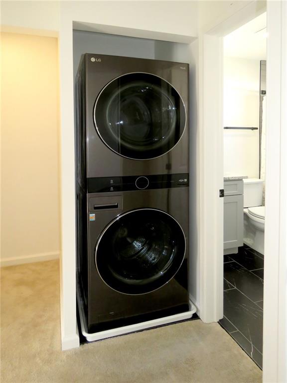 clothes washing area featuring stacked washer / dryer and light carpet