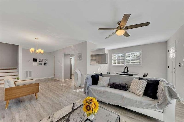 living room with ceiling fan with notable chandelier and light hardwood / wood-style floors