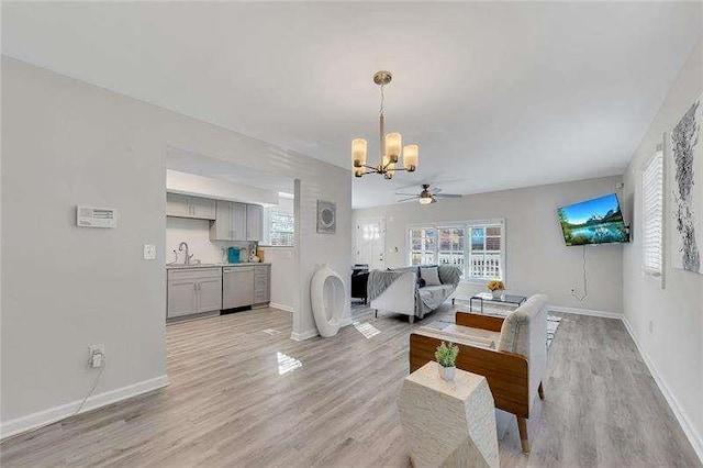 living room with ceiling fan with notable chandelier, light hardwood / wood-style floors, and sink