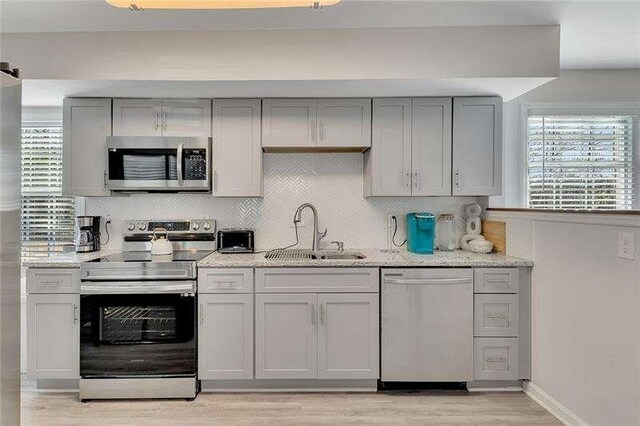 kitchen featuring gray cabinetry, backsplash, sink, appliances with stainless steel finishes, and light stone counters