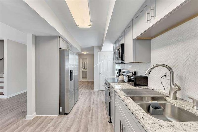 kitchen featuring light stone counters, appliances with stainless steel finishes, light hardwood / wood-style floors, and sink