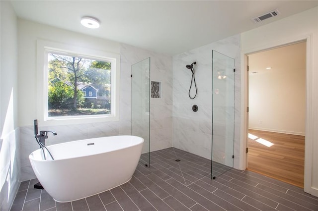 bathroom featuring visible vents, wood finished floors, walk in shower, a freestanding bath, and tile walls