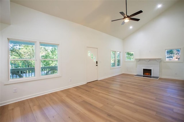 unfurnished living room with a ceiling fan, a brick fireplace, high vaulted ceiling, light wood-type flooring, and baseboards