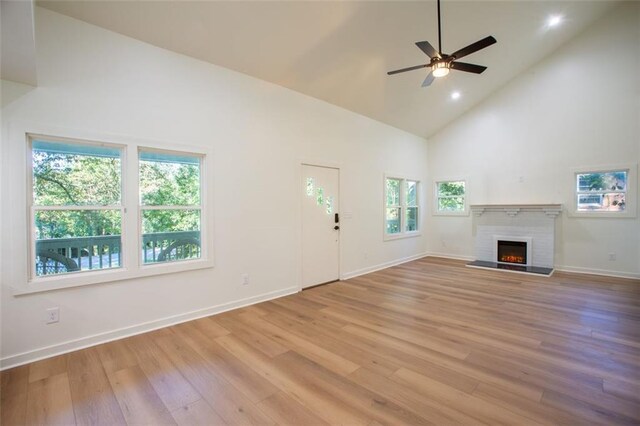 unfurnished living room featuring high vaulted ceiling, a warm lit fireplace, baseboards, and wood finished floors