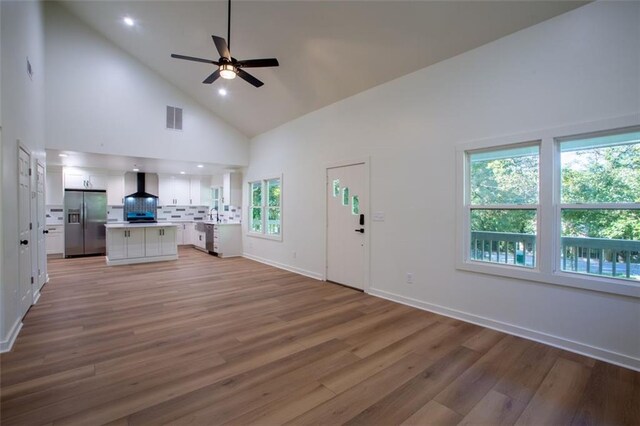 kitchen with wall chimney range hood, light wood-style flooring, appliances with stainless steel finishes, and a sink