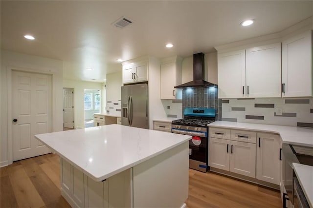 kitchen with visible vents, wall chimney exhaust hood, a center island, stainless steel appliances, and light wood-style floors