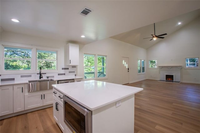 kitchen featuring stainless steel appliances, visible vents, white cabinets, a sink, and a warm lit fireplace