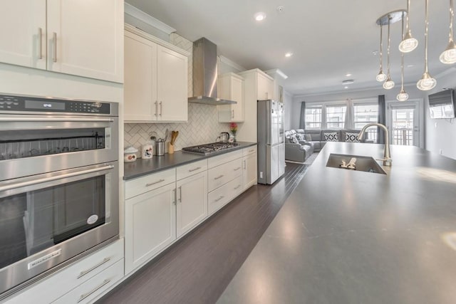 kitchen with hanging light fixtures, stainless steel appliances, sink, wall chimney exhaust hood, and tasteful backsplash