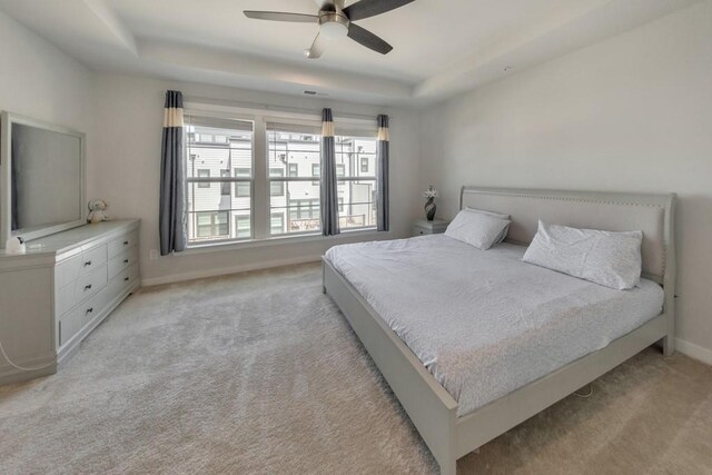 bedroom featuring a tray ceiling, light colored carpet, and ceiling fan