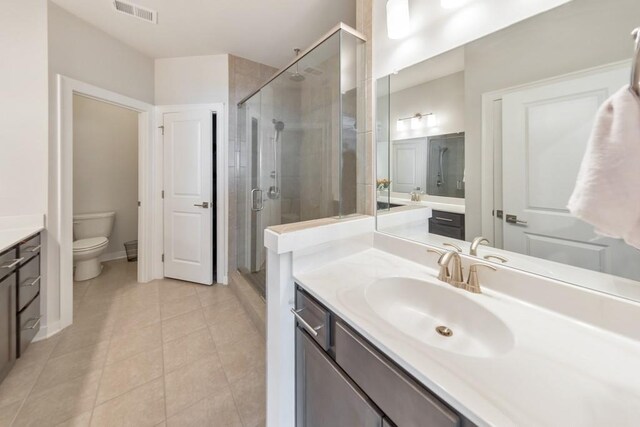 bathroom with vanity, toilet, a shower with shower door, and tile patterned flooring