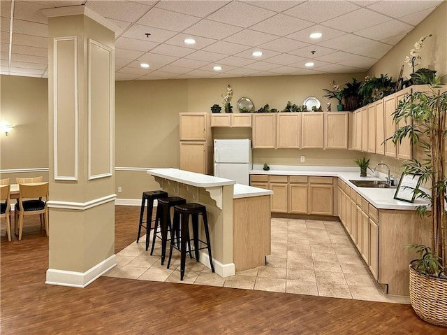 kitchen with a breakfast bar, light brown cabinetry, sink, a kitchen island, and white fridge