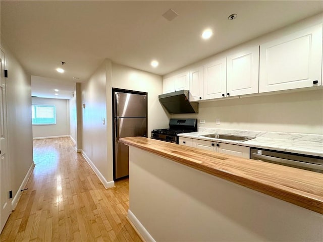 kitchen featuring wood counters, sink, white cabinets, stainless steel appliances, and light wood-type flooring