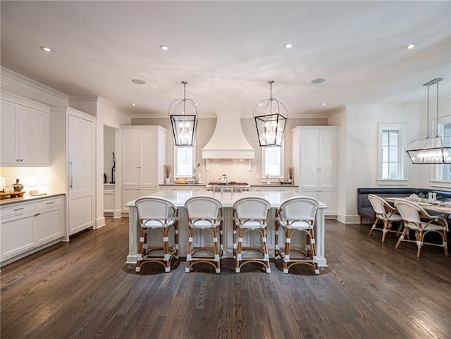 kitchen featuring custom exhaust hood, white cabinetry, dark wood-type flooring, hanging light fixtures, and a center island