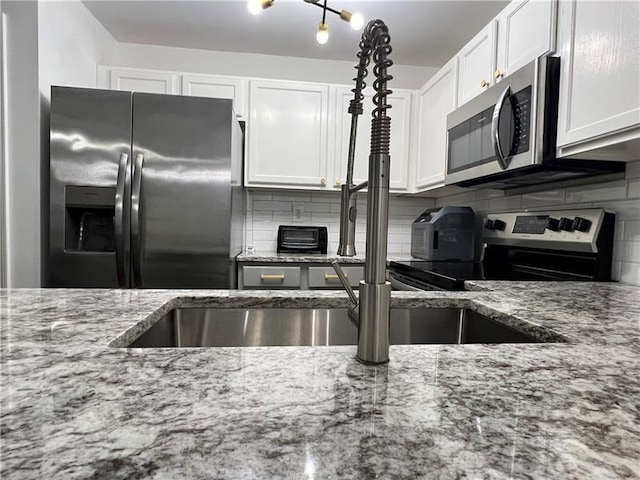 kitchen with appliances with stainless steel finishes, light stone countertops, decorative backsplash, and white cabinets