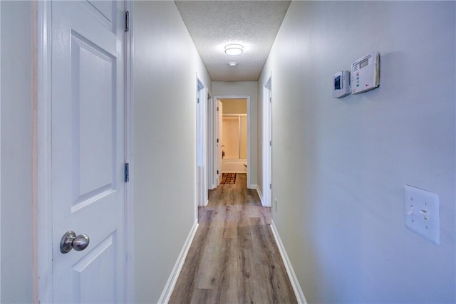 corridor with light wood finished floors, baseboards, and a textured ceiling