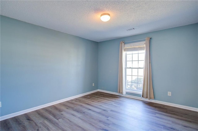 empty room with a textured ceiling, wood finished floors, visible vents, and baseboards