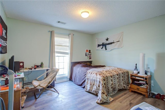 bedroom with visible vents, a textured ceiling, and wood finished floors