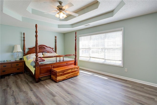 bedroom with a textured ceiling, wood finished floors, a raised ceiling, and baseboards