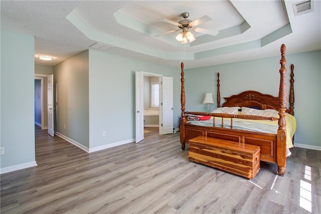 bedroom featuring a raised ceiling, a textured ceiling, baseboards, and wood finished floors