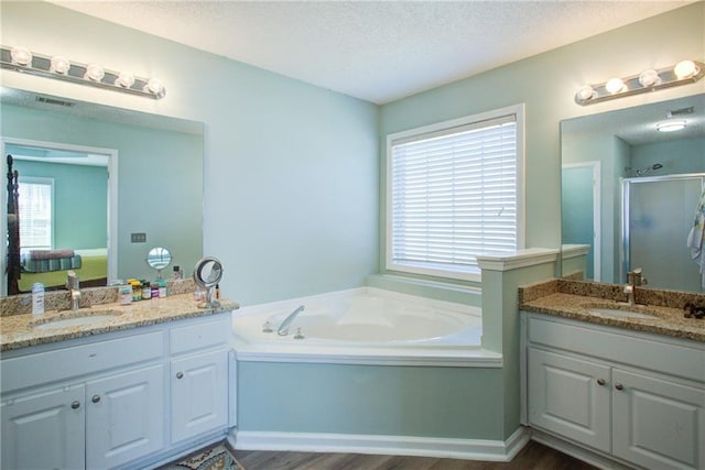 ensuite bathroom featuring a textured ceiling, two vanities, a sink, and a shower stall